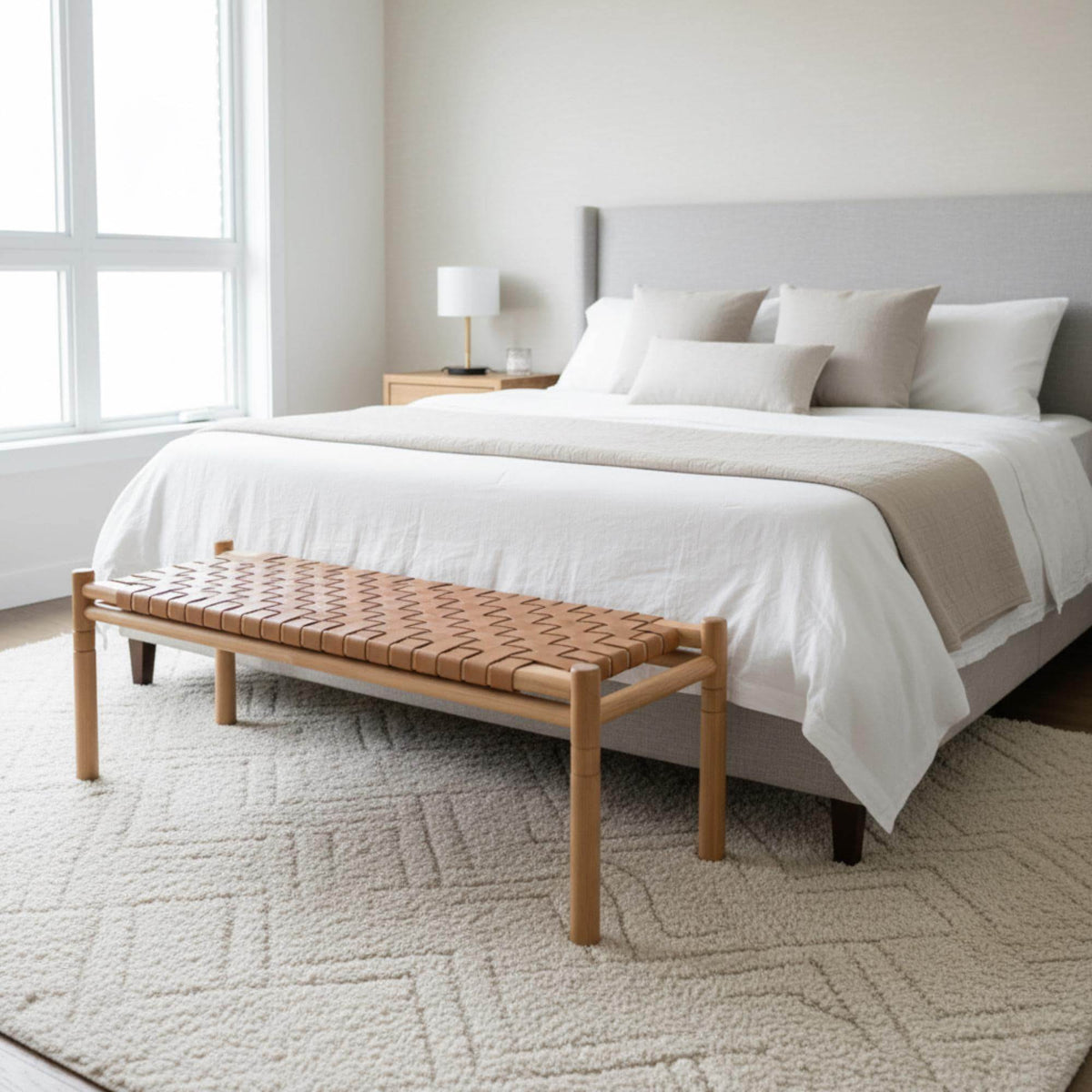 Bedroom with a bed, wooden bench, and lamp in a bright room.