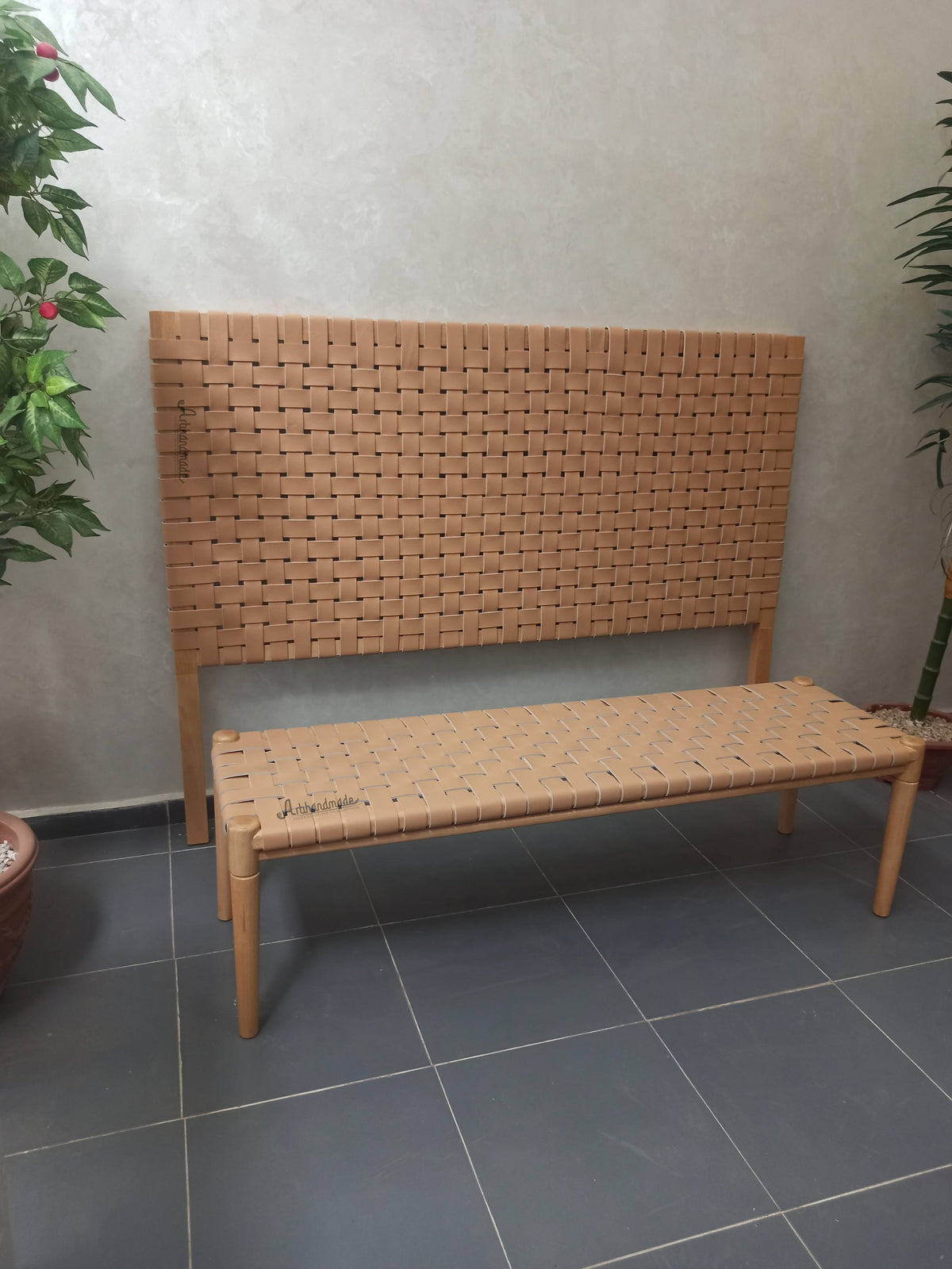 Woven bench against a plain wall with plants on either side.