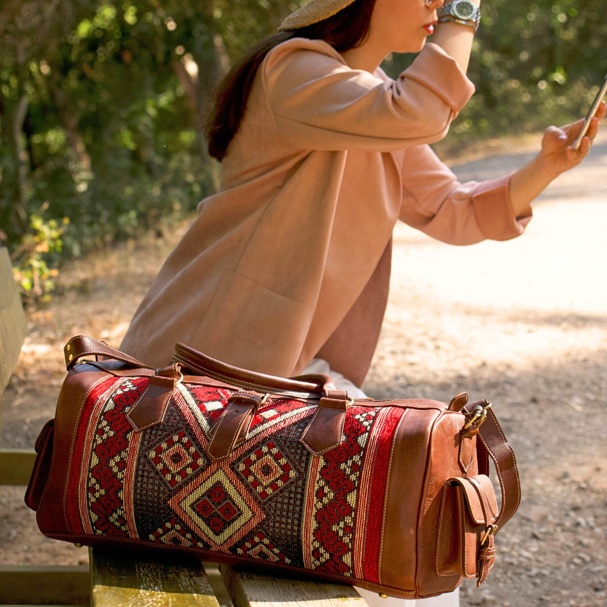 A person sitting outdoors with a leather kilim travel duffel bag featuring a geometric kilim design in brown and black colors.