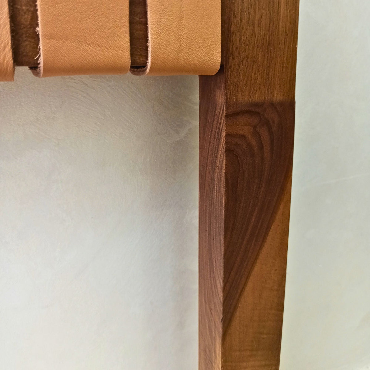 Close-up of a walnut wood shelf with a leather strap on a light background